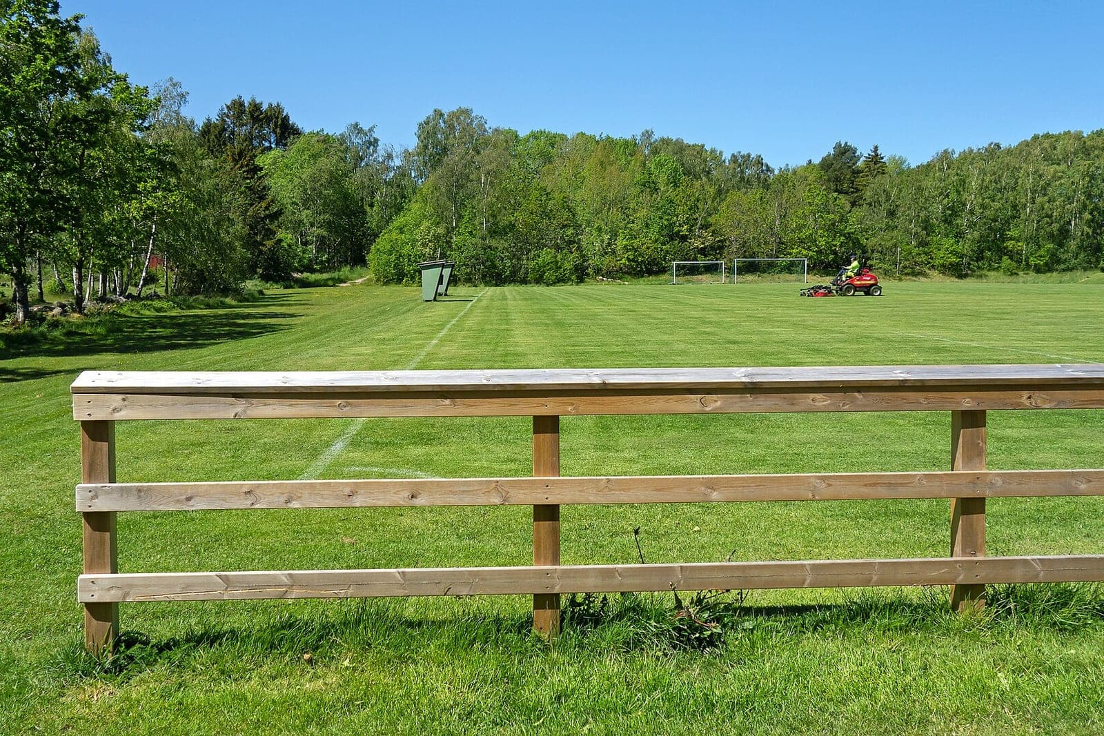A wooden rail fence in front of a large mowed field with a riding mower in the distance