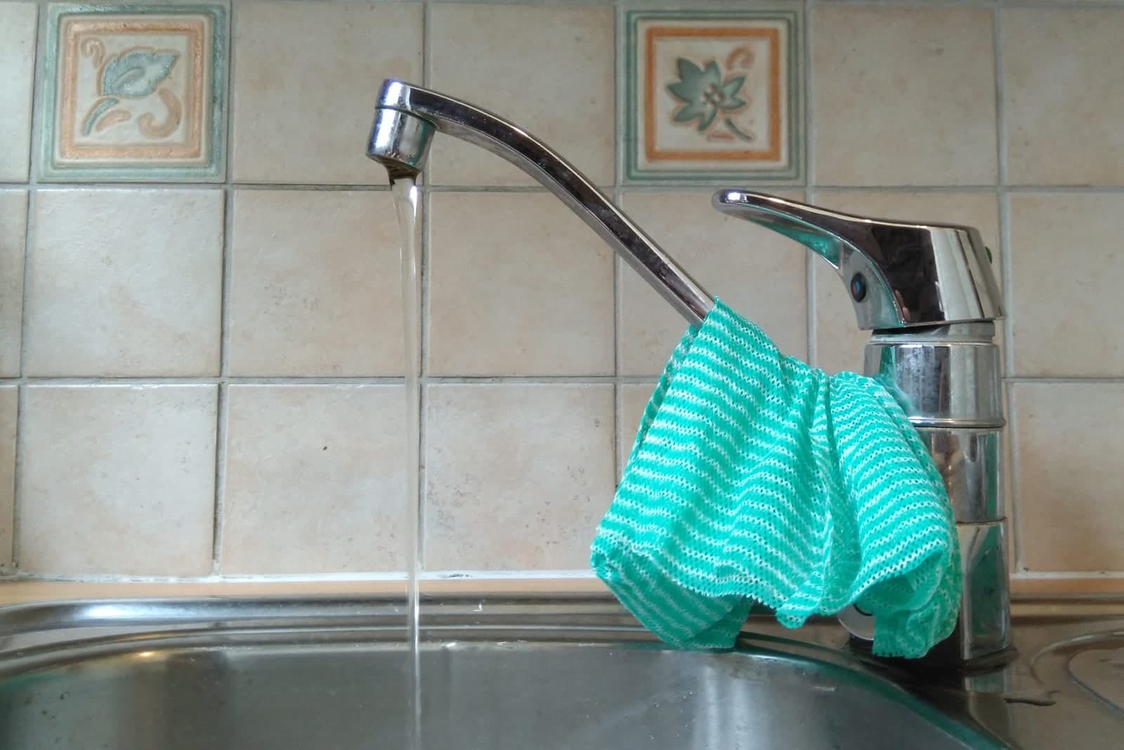 Water running from a chrome single-handle kitchen faucet into a steel sink, a cloth over the spout