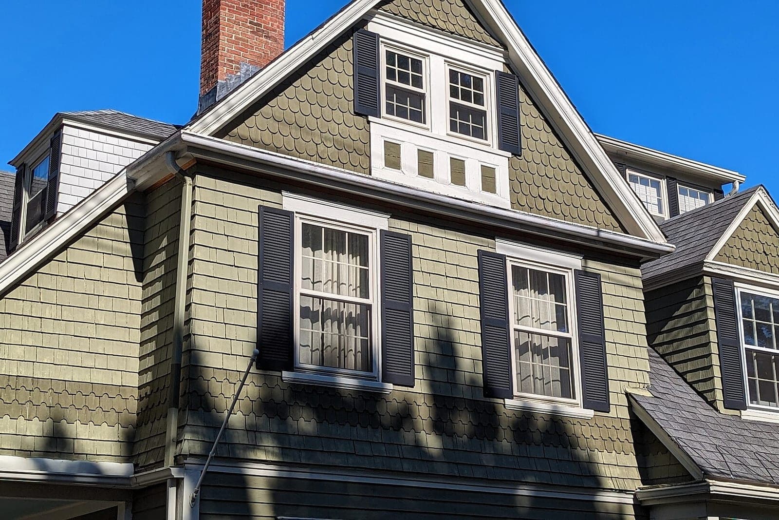 A two-story house with shingle siding, dark shutters and a gray shingle roof
