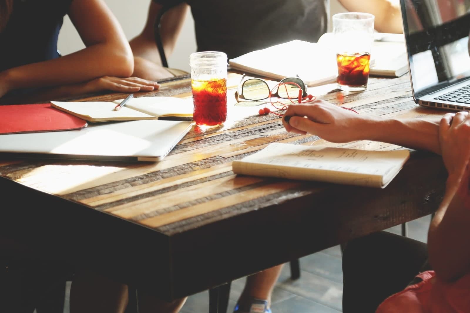 People work through notebooks and laptops together at a wooden table