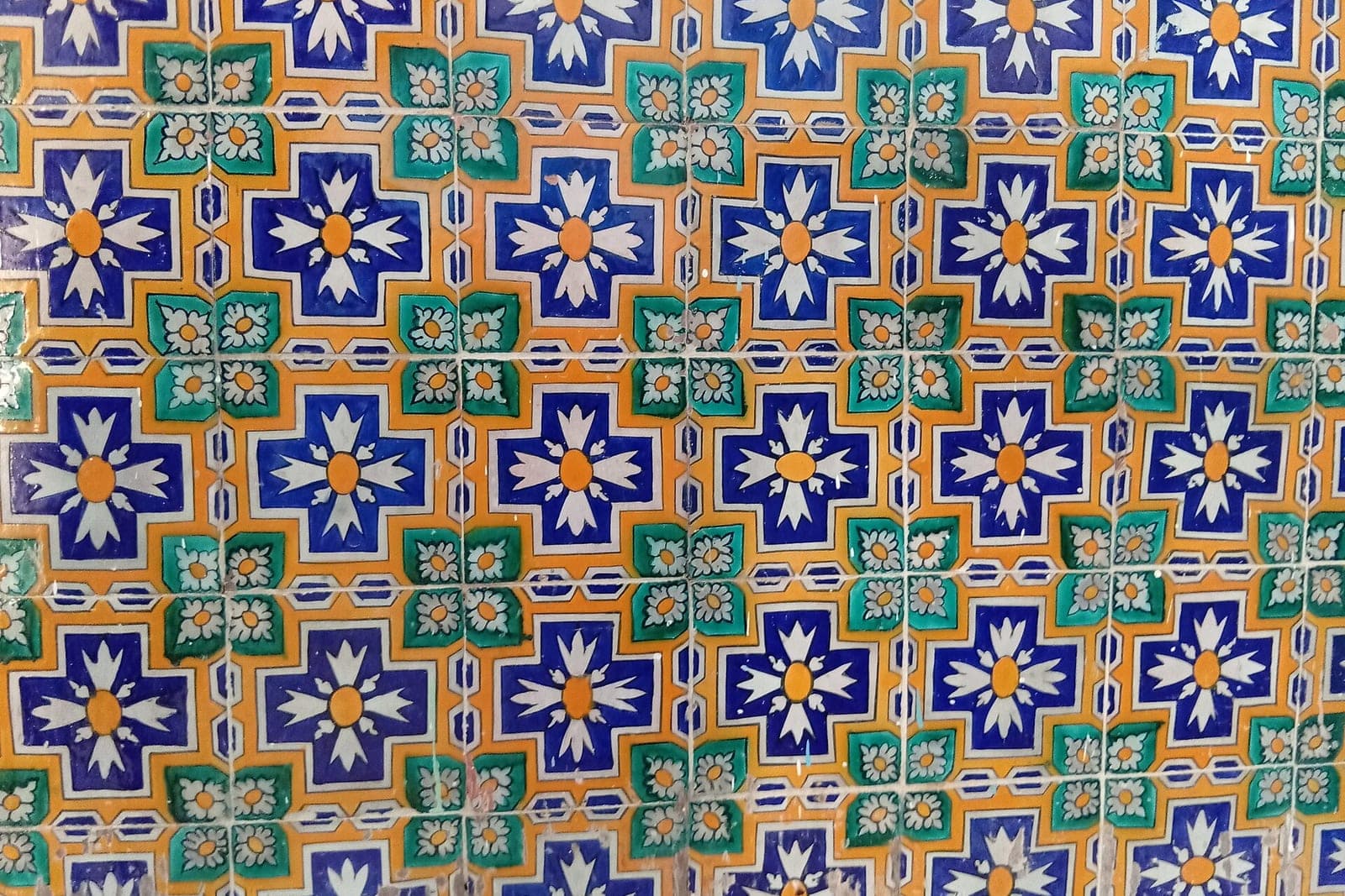 A wall of hand-painted ceramic tiles in blue, green and orange cross and flower patterns