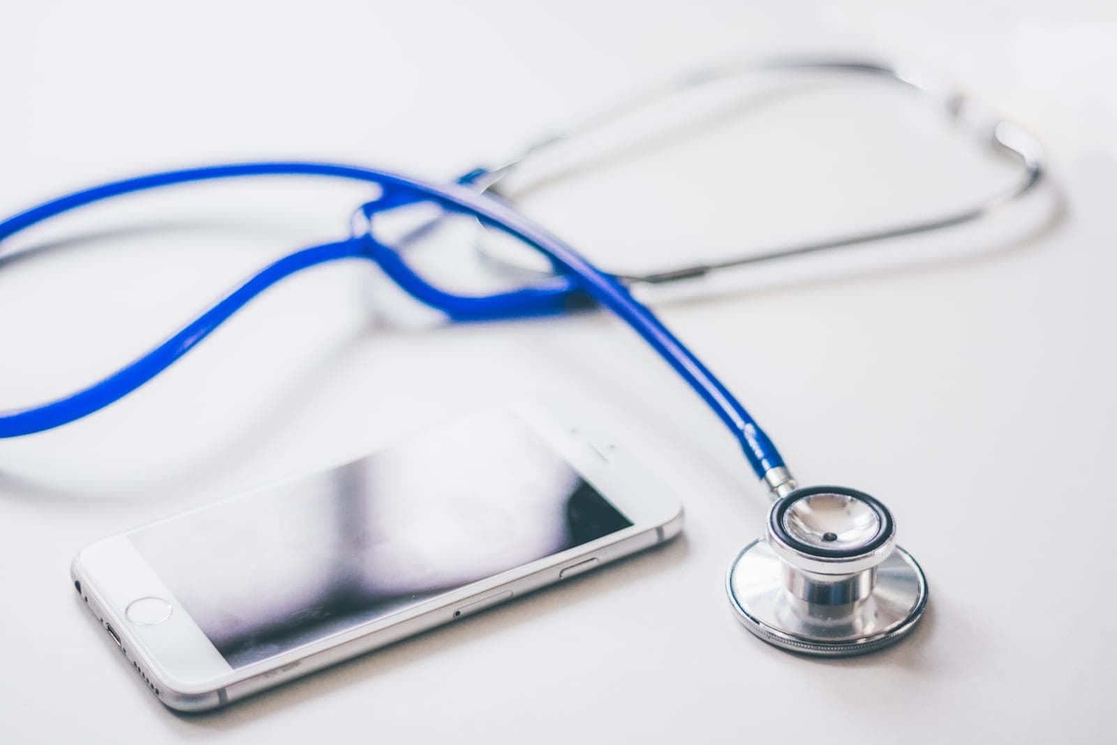 A blue stethoscope lying beside a smartphone on a white table
