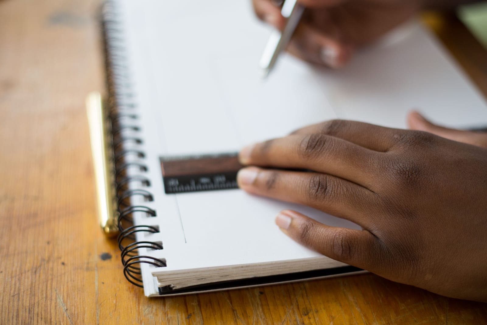 A hand holds a ruler steady while drawing a precise line in a spiral notebook