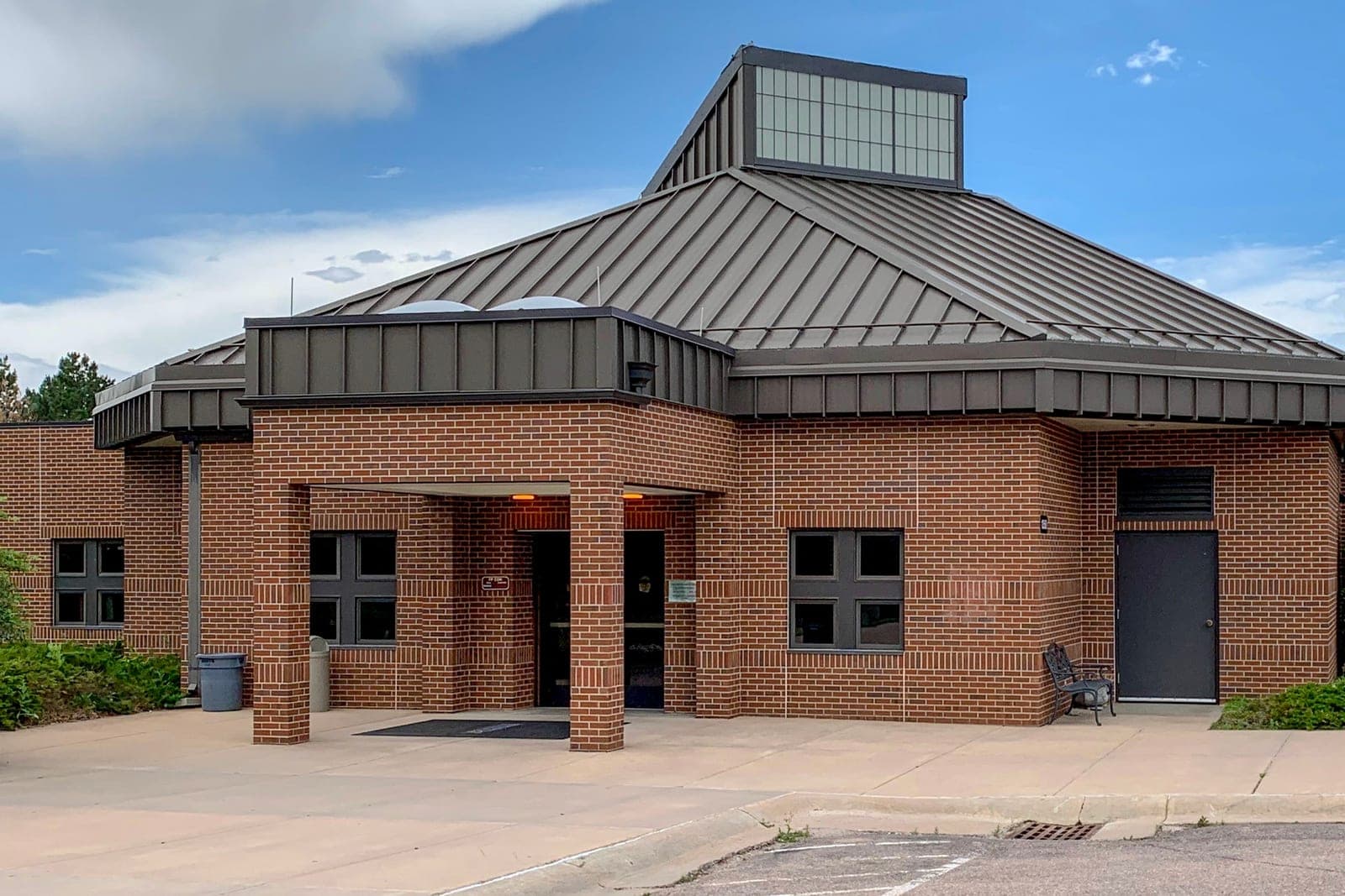 A one-story brick child care center with a covered front entrance and a metal roof under a blue sky