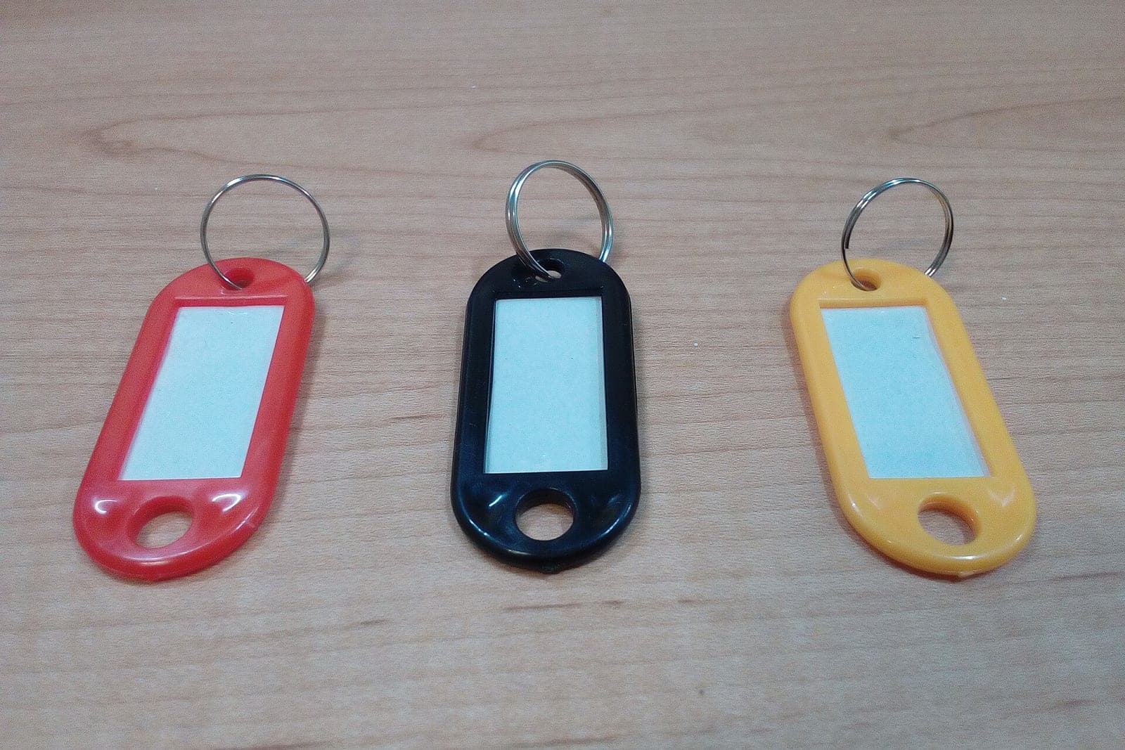Three blank plastic key tags in red, black and yellow on a wooden desk