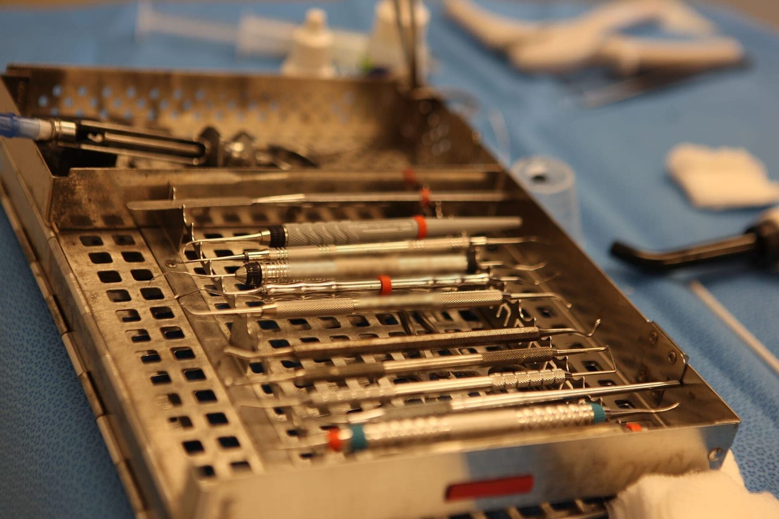 Steel dental hand instruments lined up in a perforated tray on a blue drape
