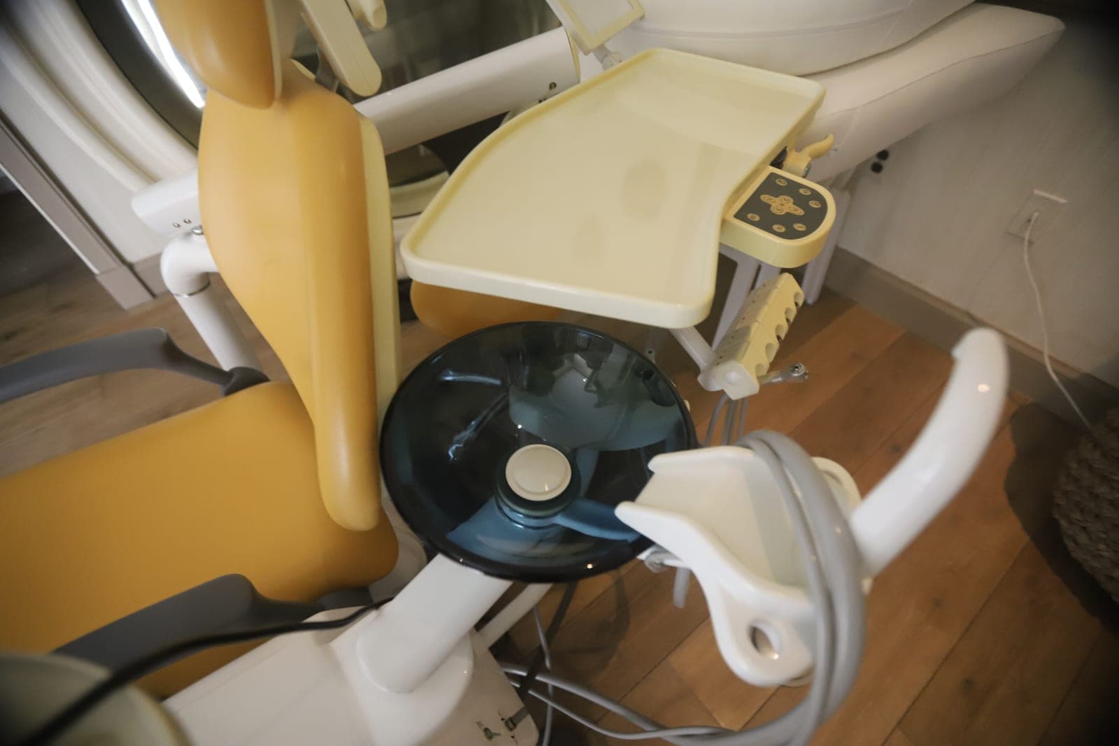 An empty yellow dental chair with its tray and light arm in a treatment room with a wooden floor