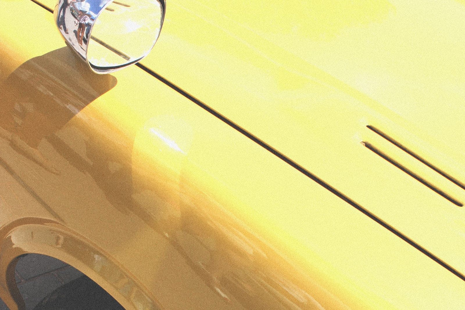 The chrome mirror, front fender and wheel arch of a bright yellow car in sunlight
