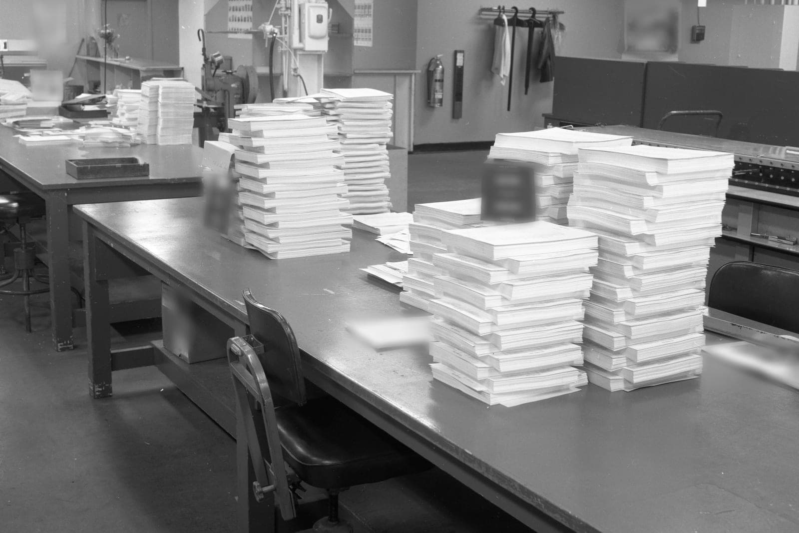 Tall, neat stacks of paper documents waiting on long work tables in an office