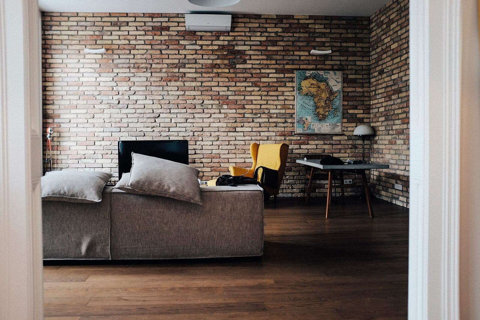 A living room with a brick wall, a gray sofa and a wall unit near the ceiling
