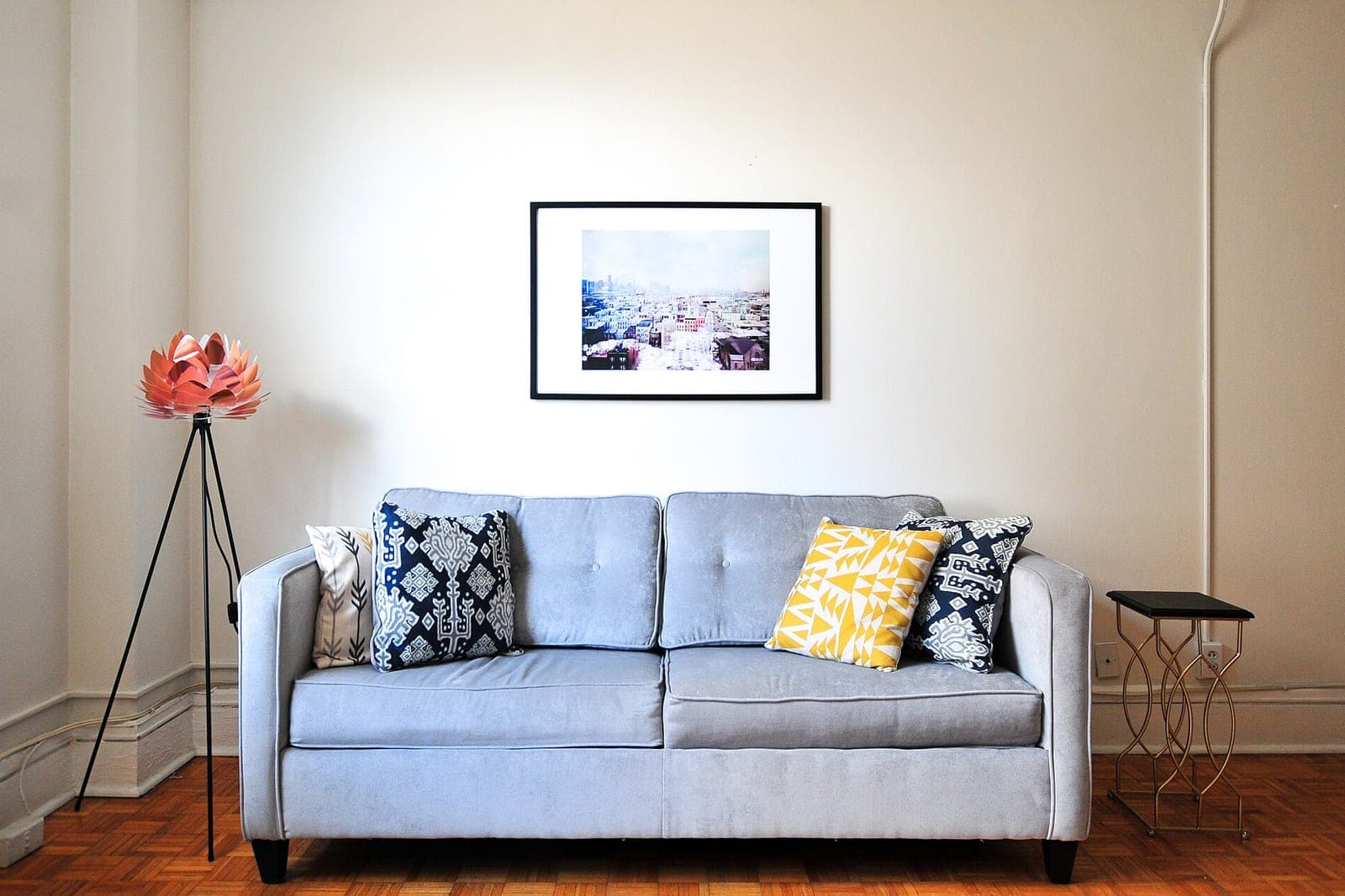 A light gray sofa with patterned pillows under a framed print in a bright room