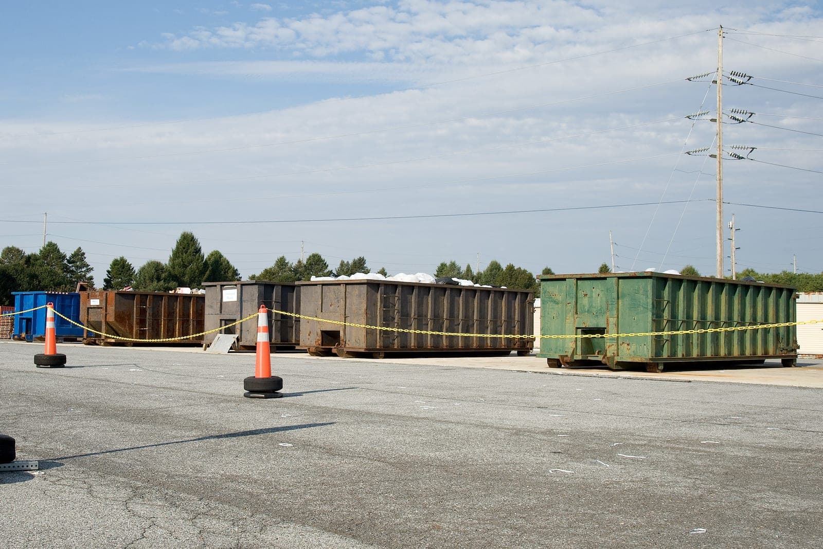 Roll-off containers stand in a row behind orange cones on a wide paved lot