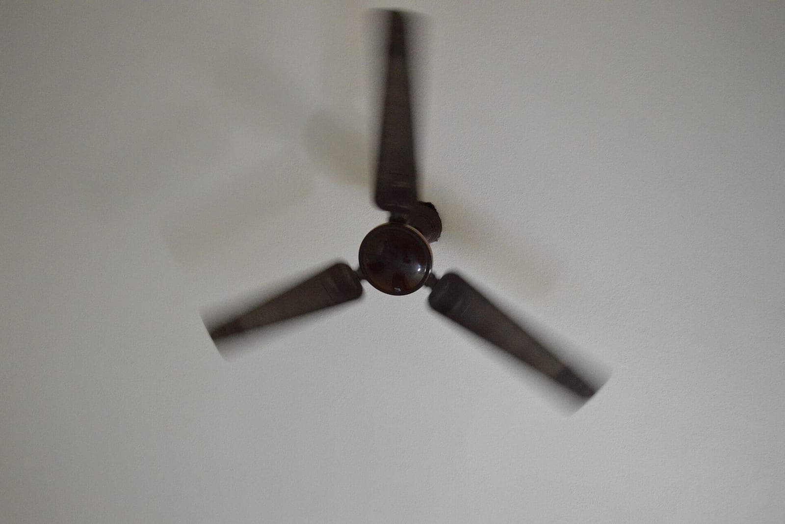 A dark ceiling fan with three blades spinning against a white ceiling