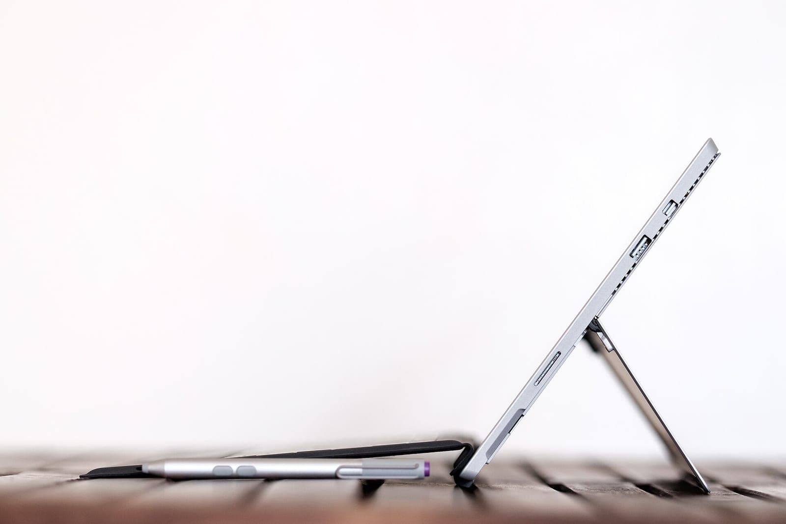 A thin silver tablet stands on its kickstand on a wooden table beside a stylus