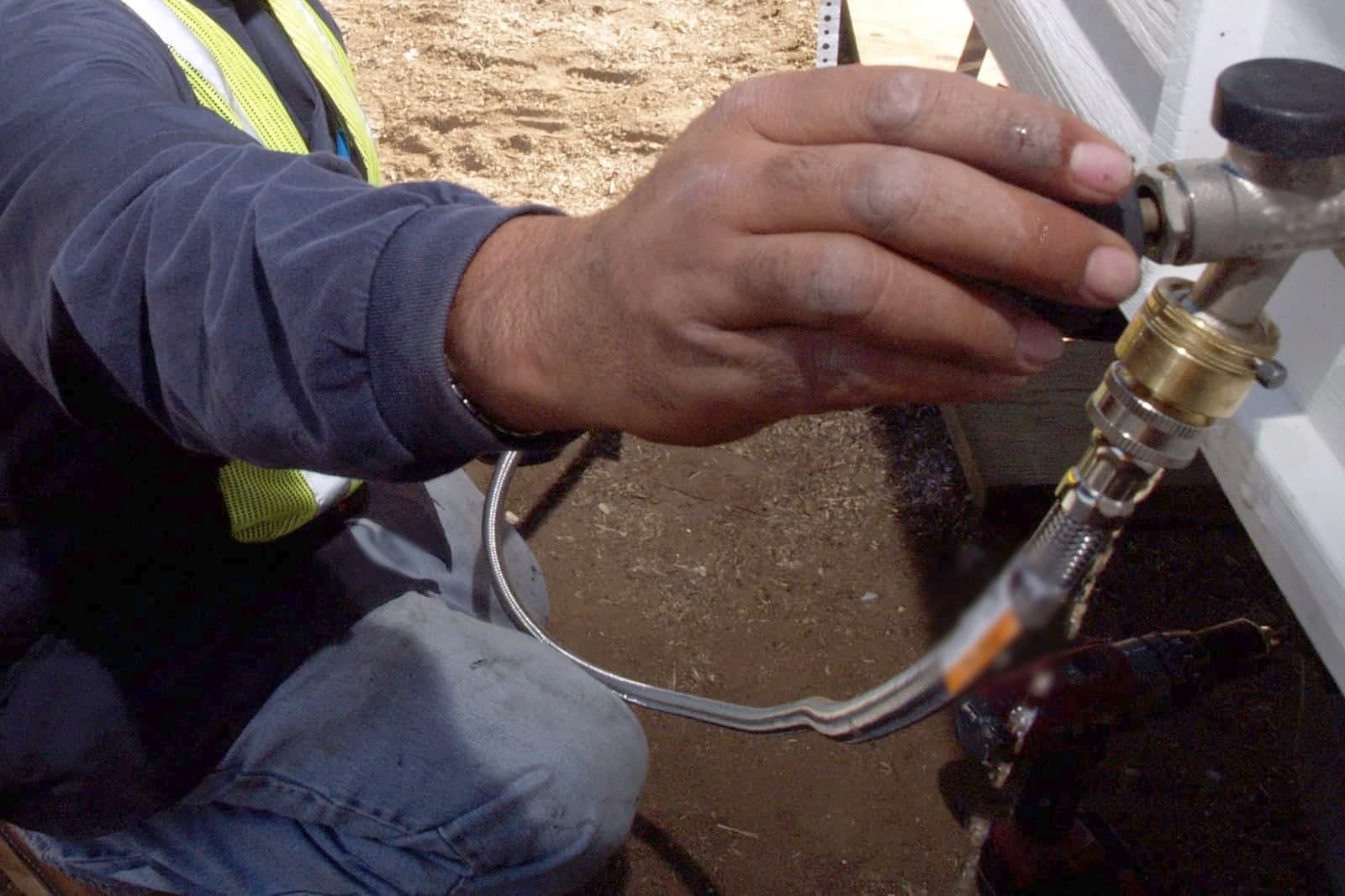 A service tech in a safety vest reaches out to connect a water line on the side of a home during a job