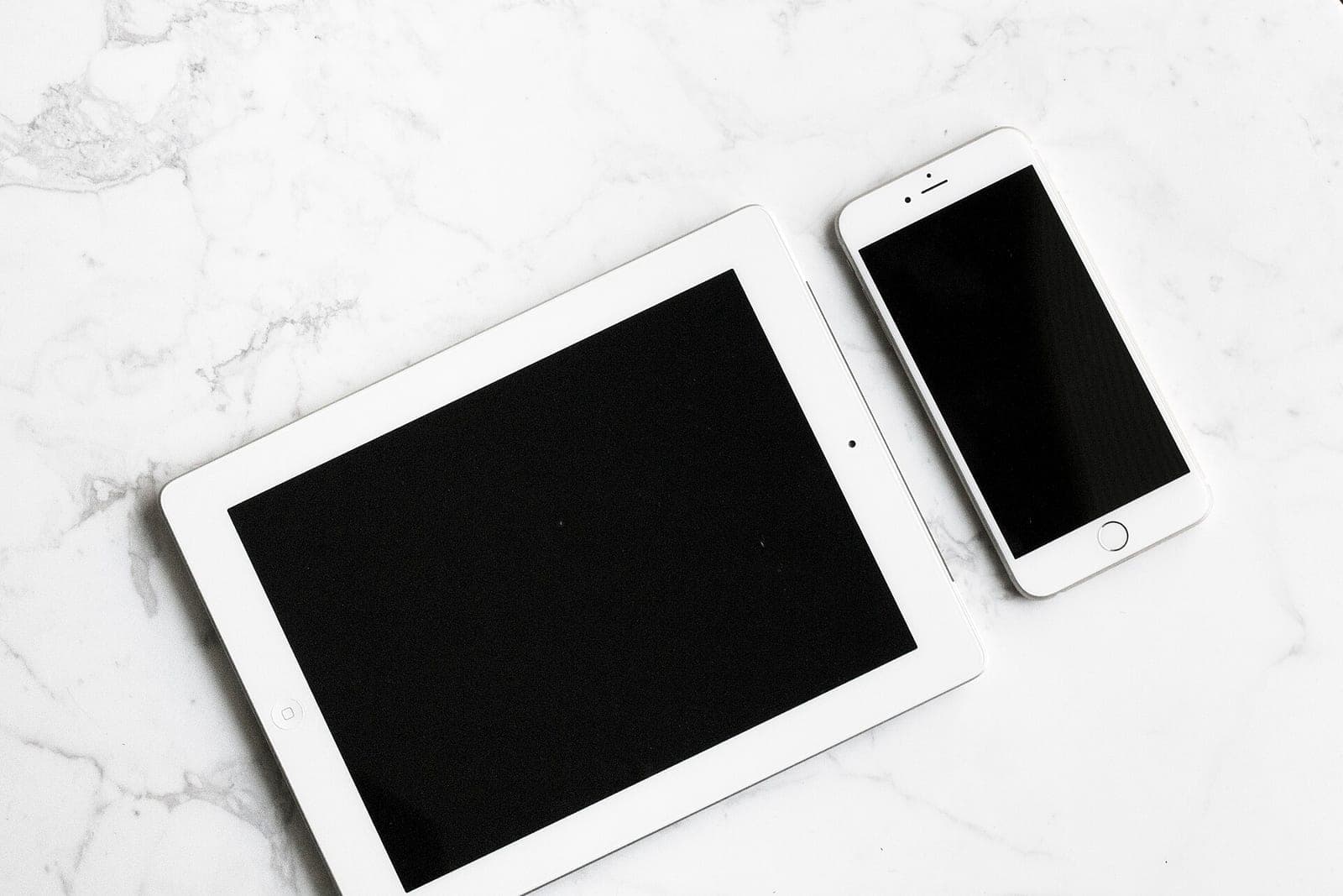 A white tablet and a white phone lie side by side on a marble countertop