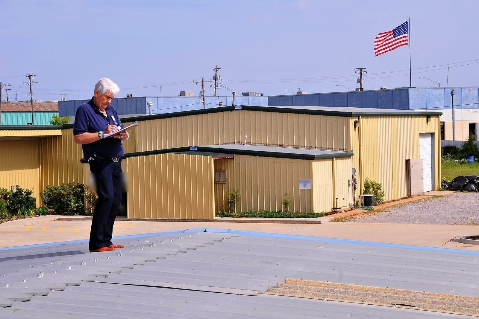 A man with a clipboard writes notes while standing on a metal roof