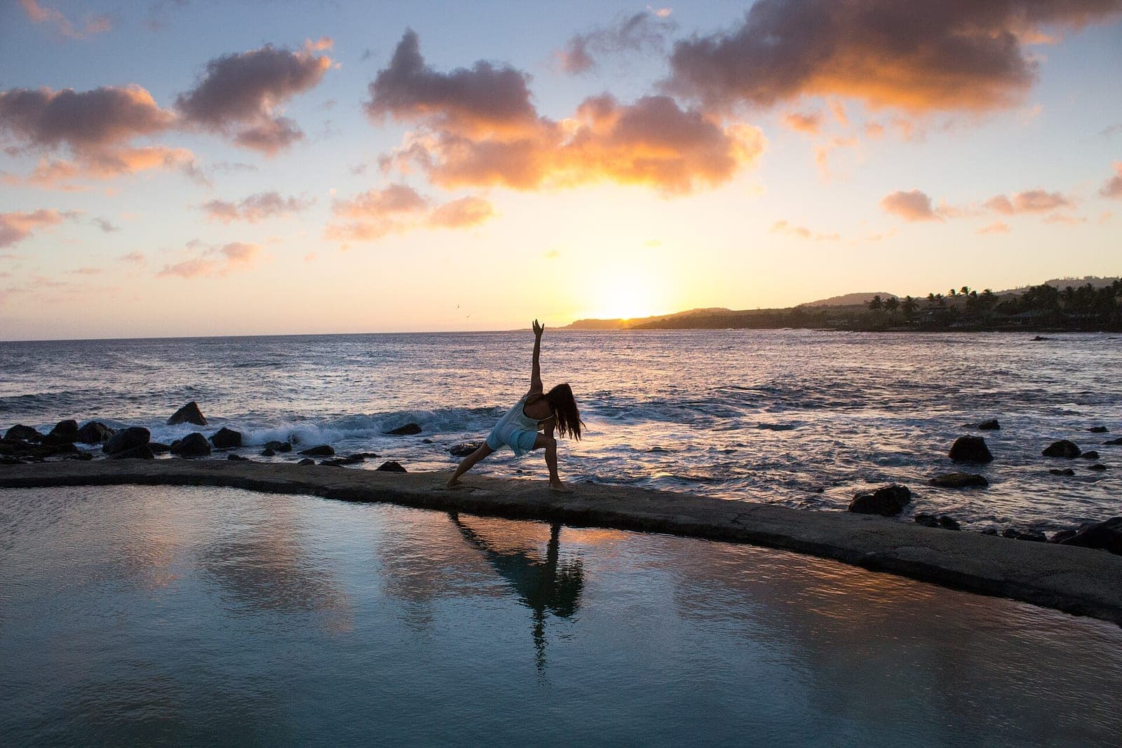 A person in a side stretch on a stone ledge by the sea at sunset