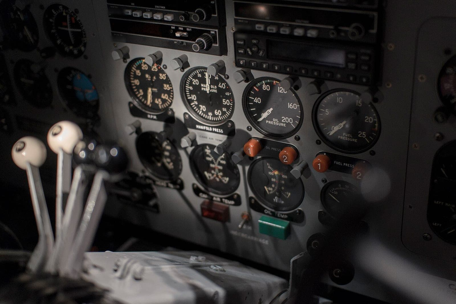 The instrument panel of a small propeller airplane with round engine gauges and white-knobbed throttle levers