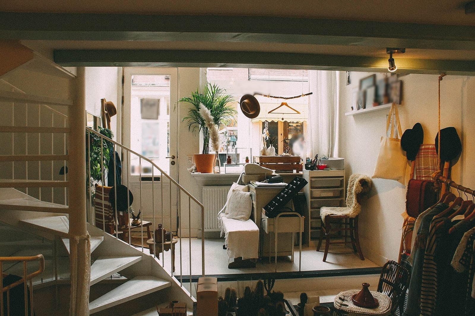 A small shop with a spiral staircase, a potted palm by the front window and clothes on a rack