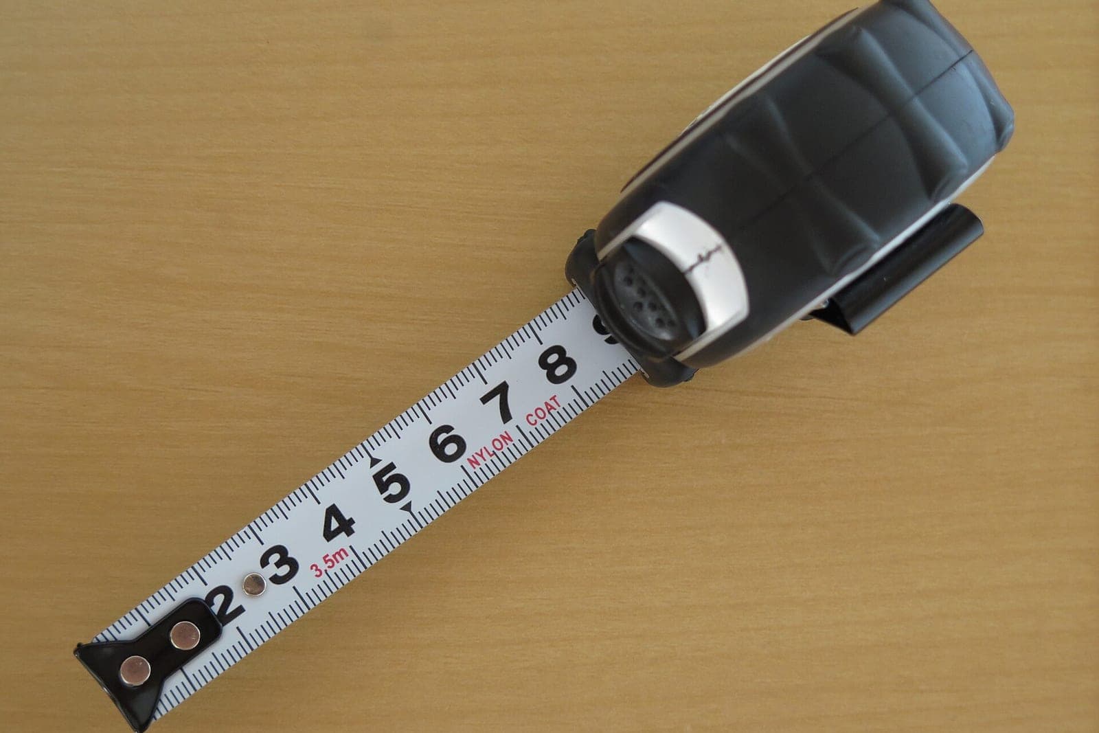 A black tape measure pulled out across a wooden table
