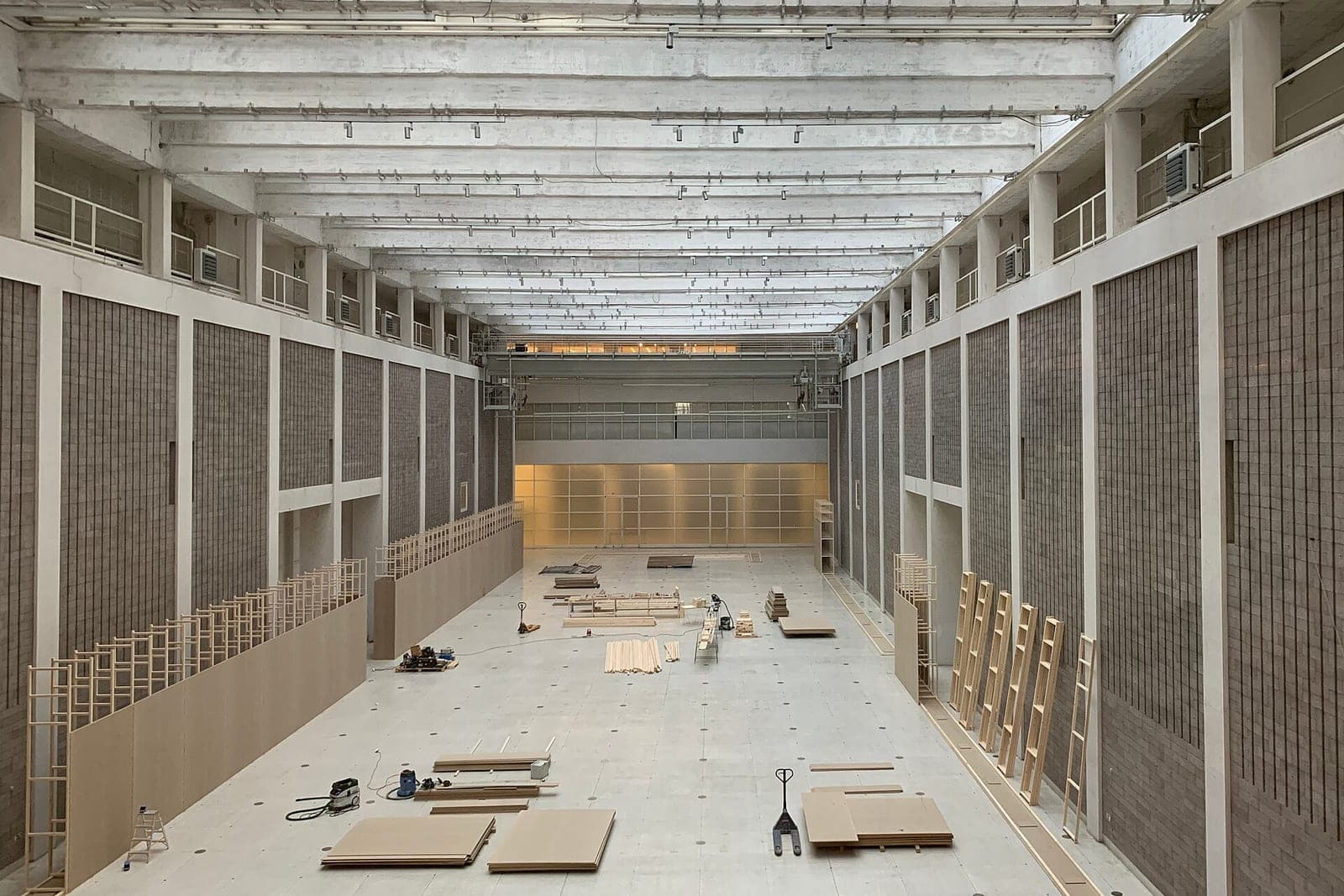 An empty hall under renovation with lumber, ladders and panels on the floor