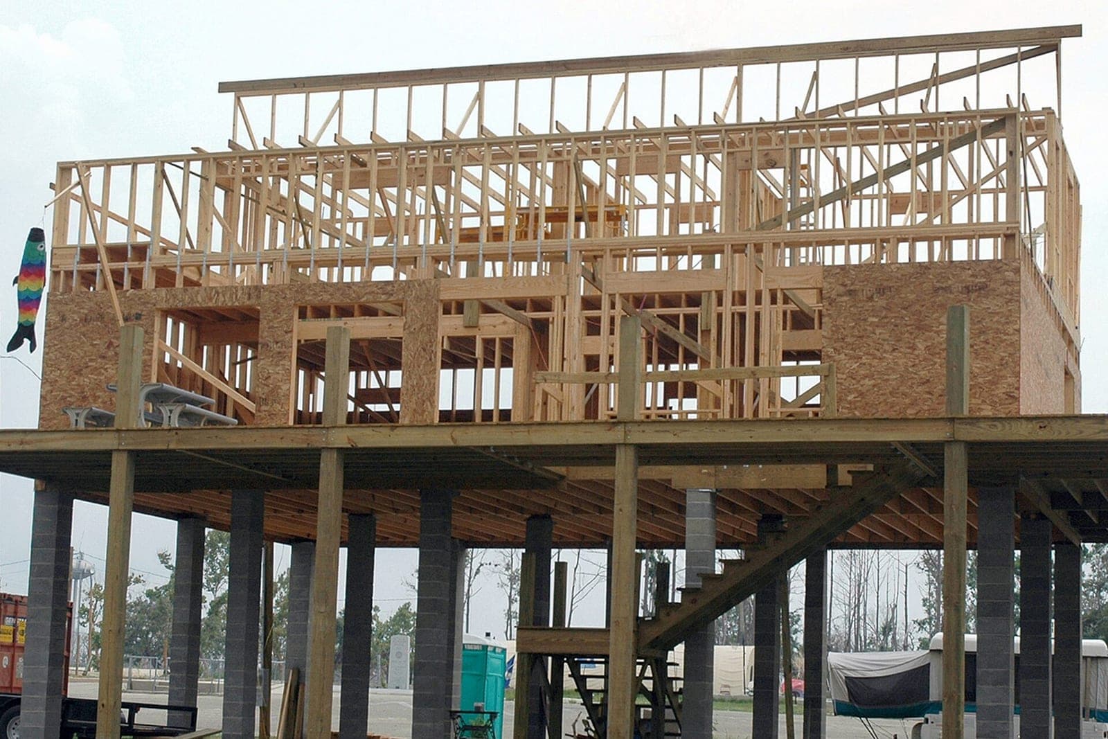 The wood frame of a new two-story house stands on a raised platform of block piers