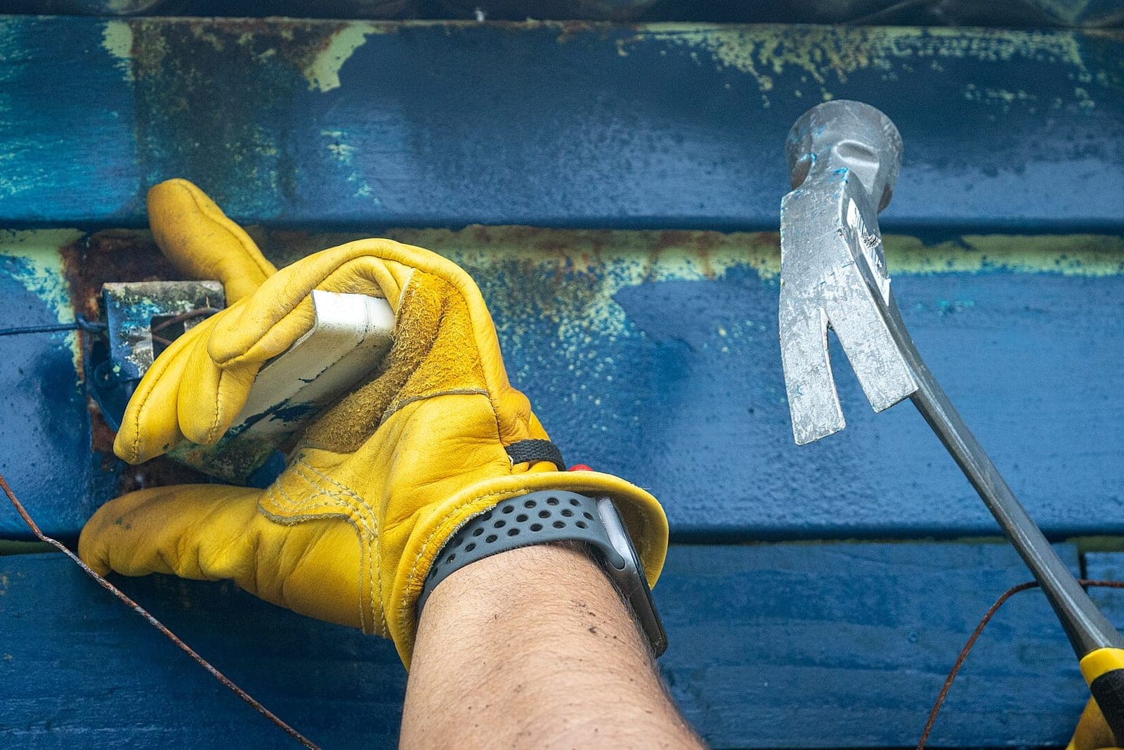 A gloved hand fixing a bracket to blue painted wood siding beside a hammer