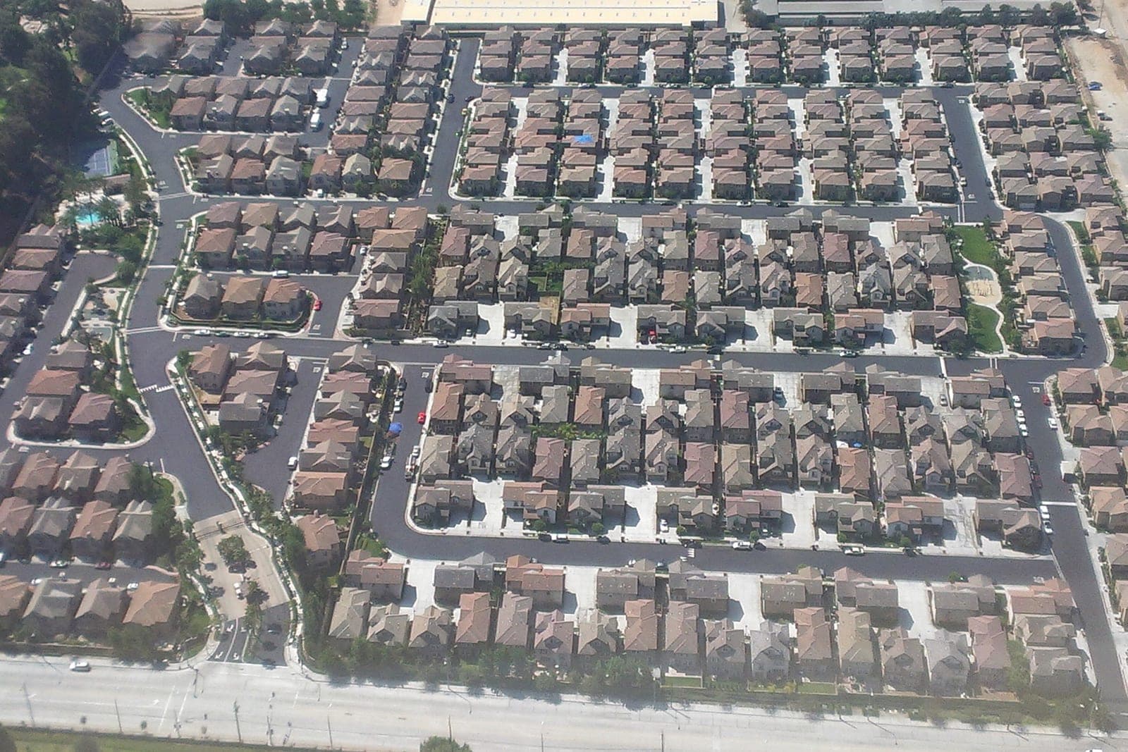 An aerial view of a planned neighborhood with rows of similar two-story homes, curving streets, a pool and a small park