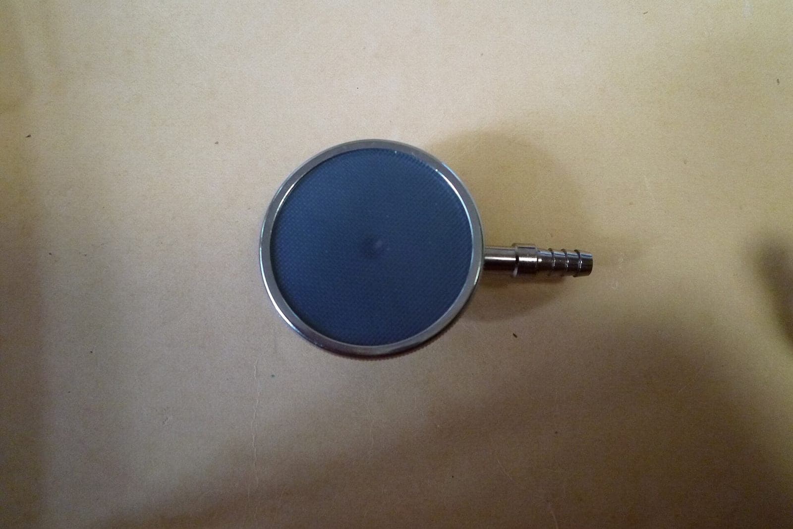 The round metal chestpiece of a stethoscope lying on a sheet of tan paper