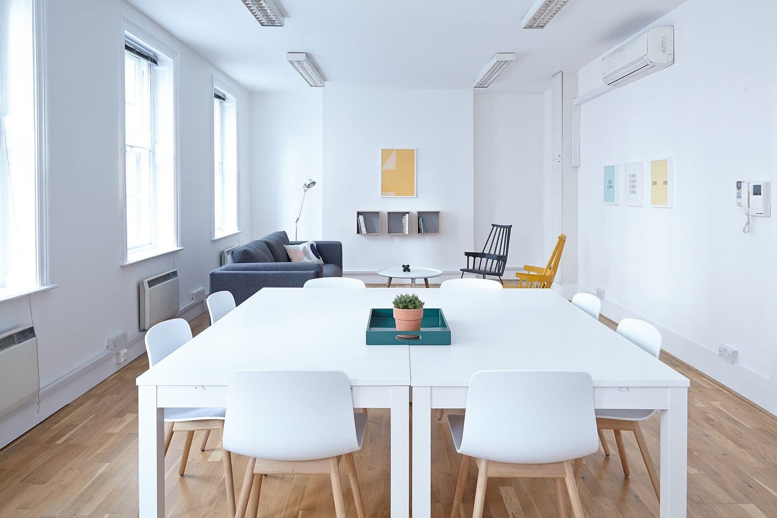 A bright meeting room with a white table, white chairs and a wooden floor
