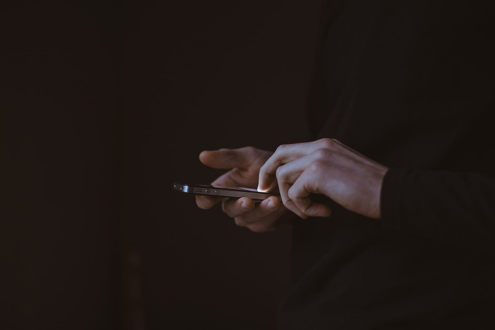 One hand holds a smartphone while the other taps it, against a dark background