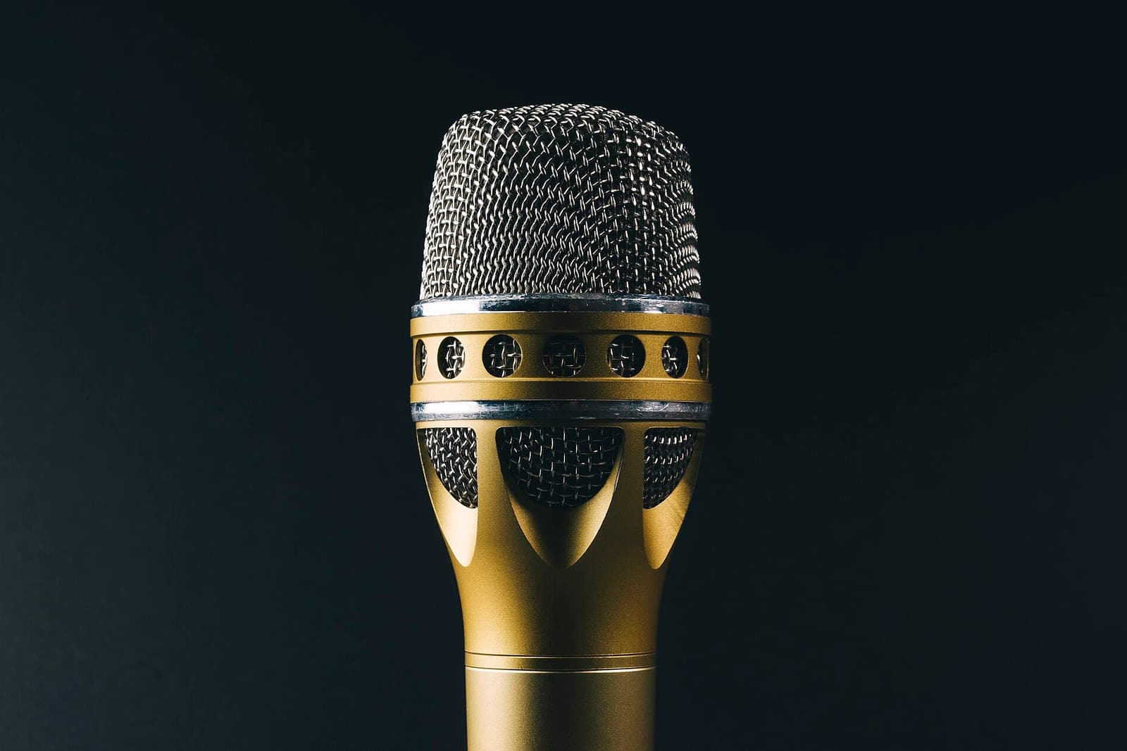 A gold handheld microphone with a silver mesh head against a dark background