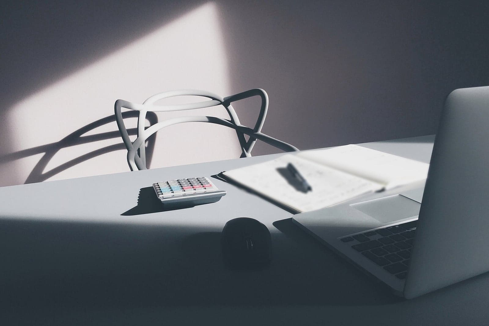 A calculator, an open notebook and a laptop on a sunlit desk