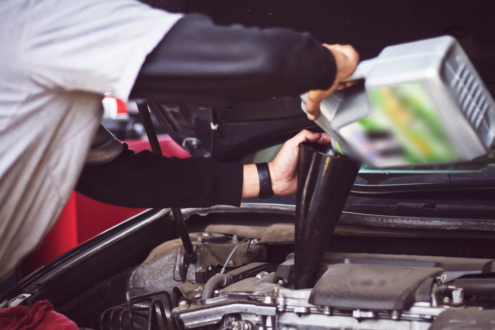 A mechanic's hands pour fresh oil through a funnel into a car engine under the open hood