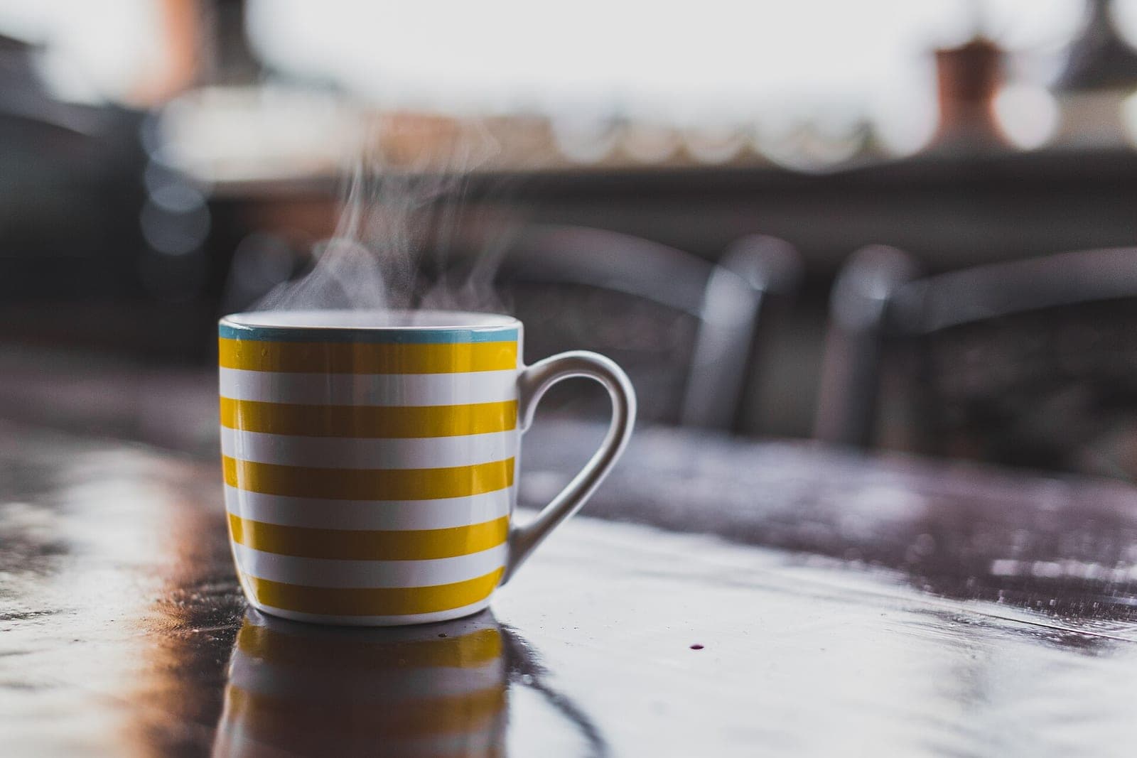 A steaming yellow-and-white striped mug on a dark wooden cafe table