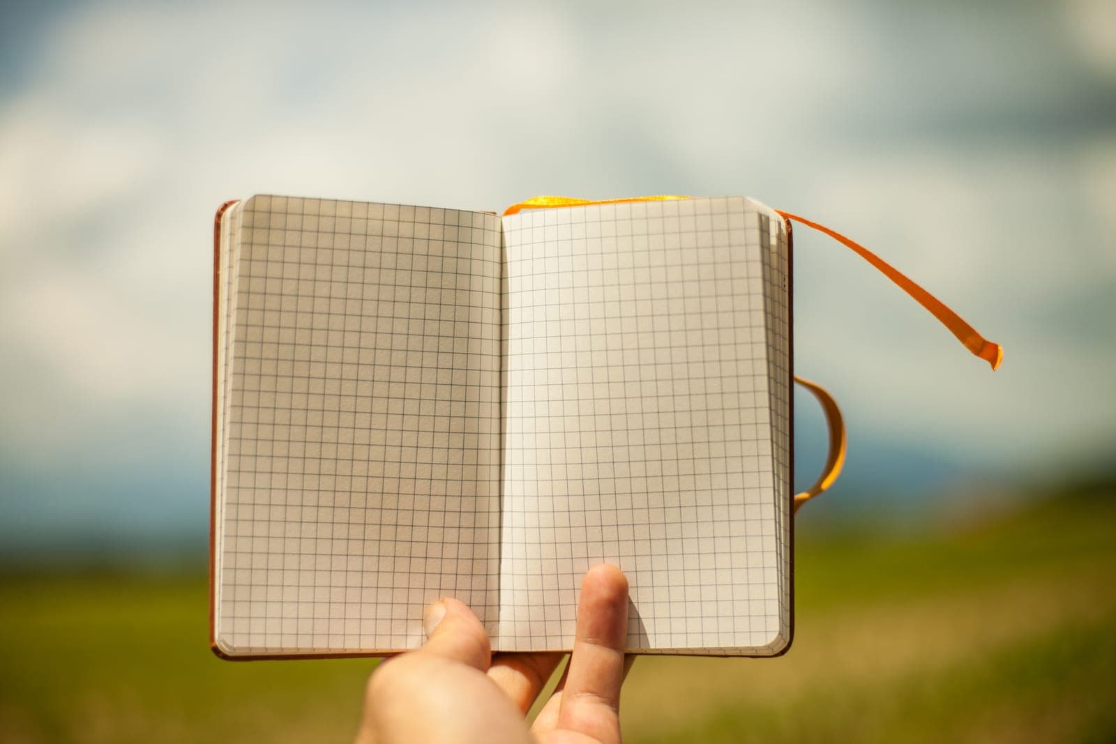 Hand holding an open notebook with blank grid pages, ready to map out the day's work