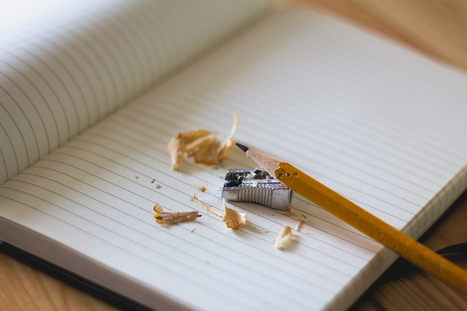 A sharpened yellow pencil, a metal sharpener and pencil shavings on a blank lined notebook page