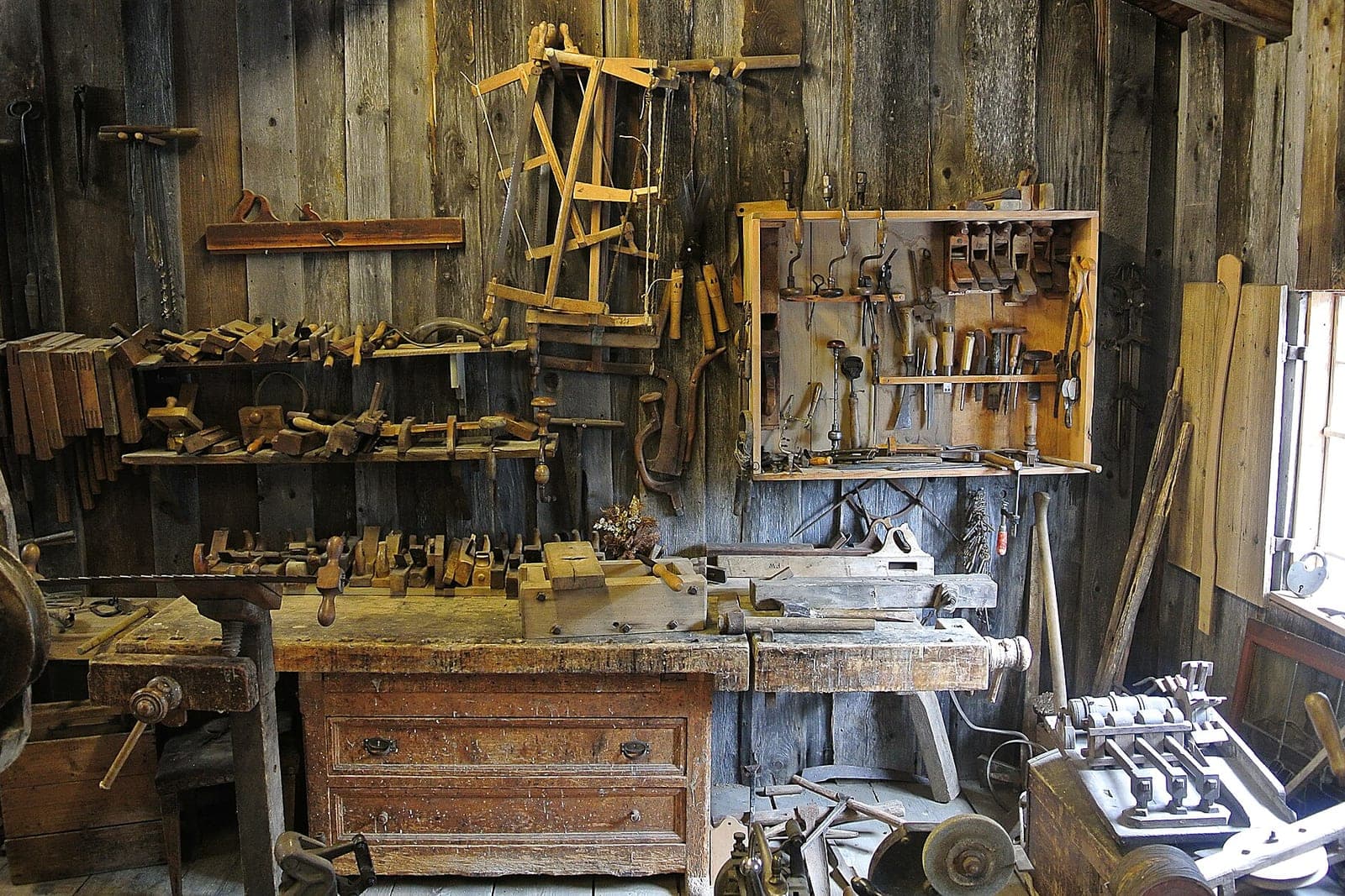 A wooden workbench with hand tools hung in neat rows on the wall above it