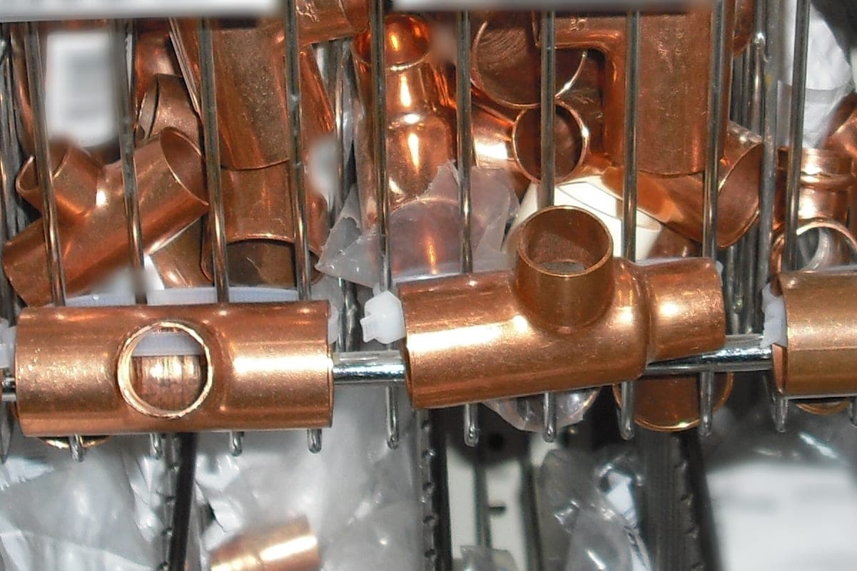 Copper tee fittings hanging on a rail in front of wire bins full of more fittings