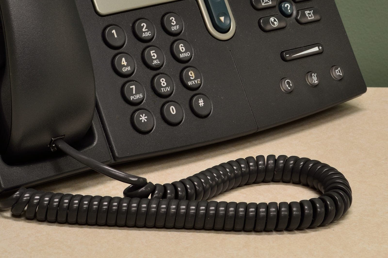 The keypad and coiled cord of a black office desk phone on a light desk