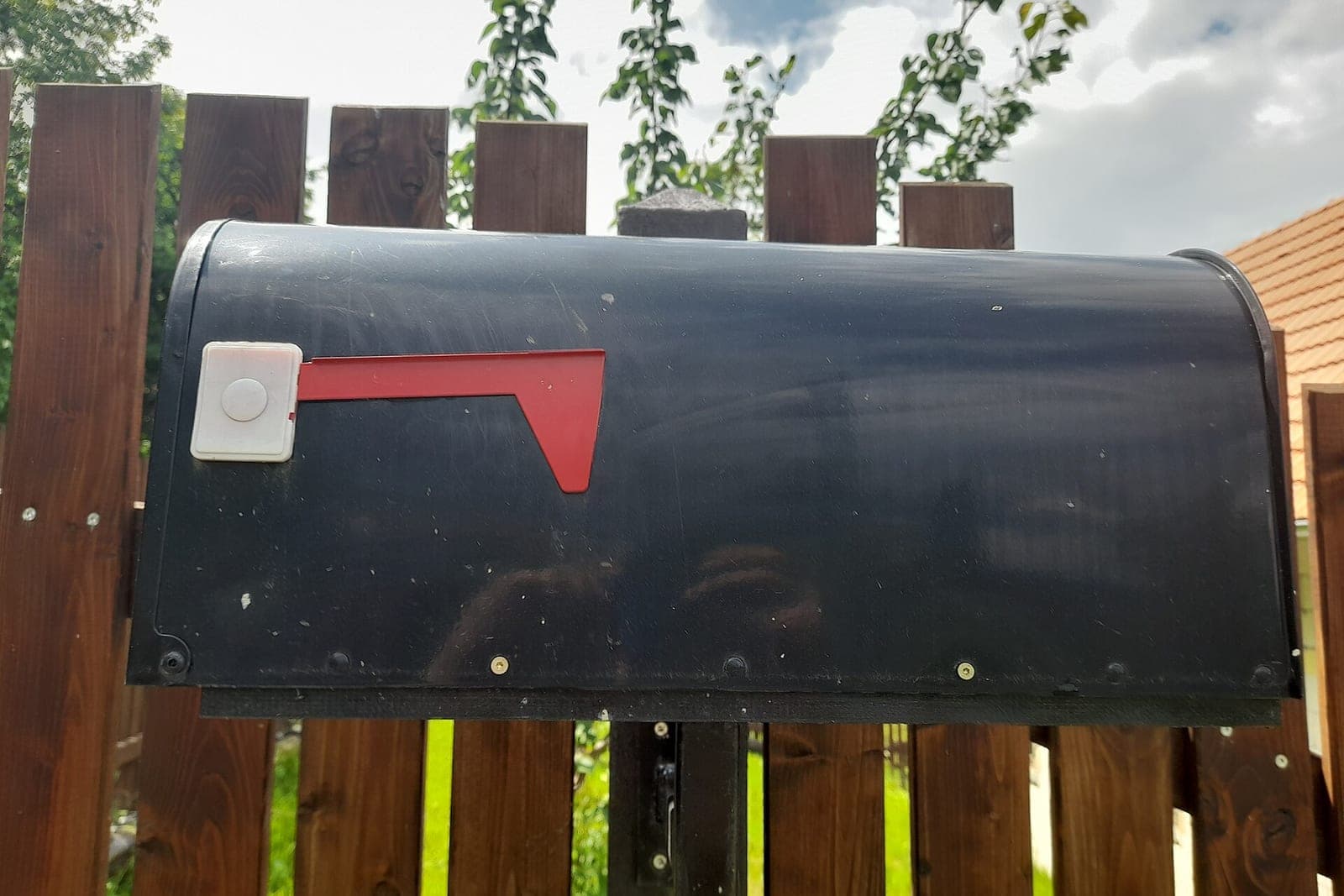 A black mailbox with a red flag mounted on a wooden fence