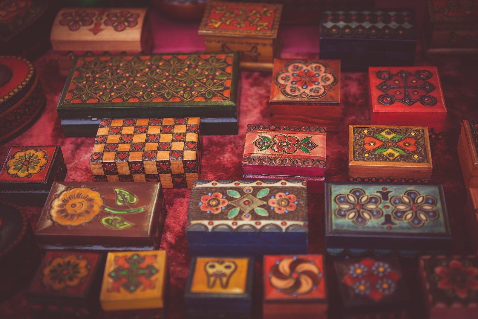Rows of hand-painted wooden boxes with flower patterns laid out for sale on a red cloth