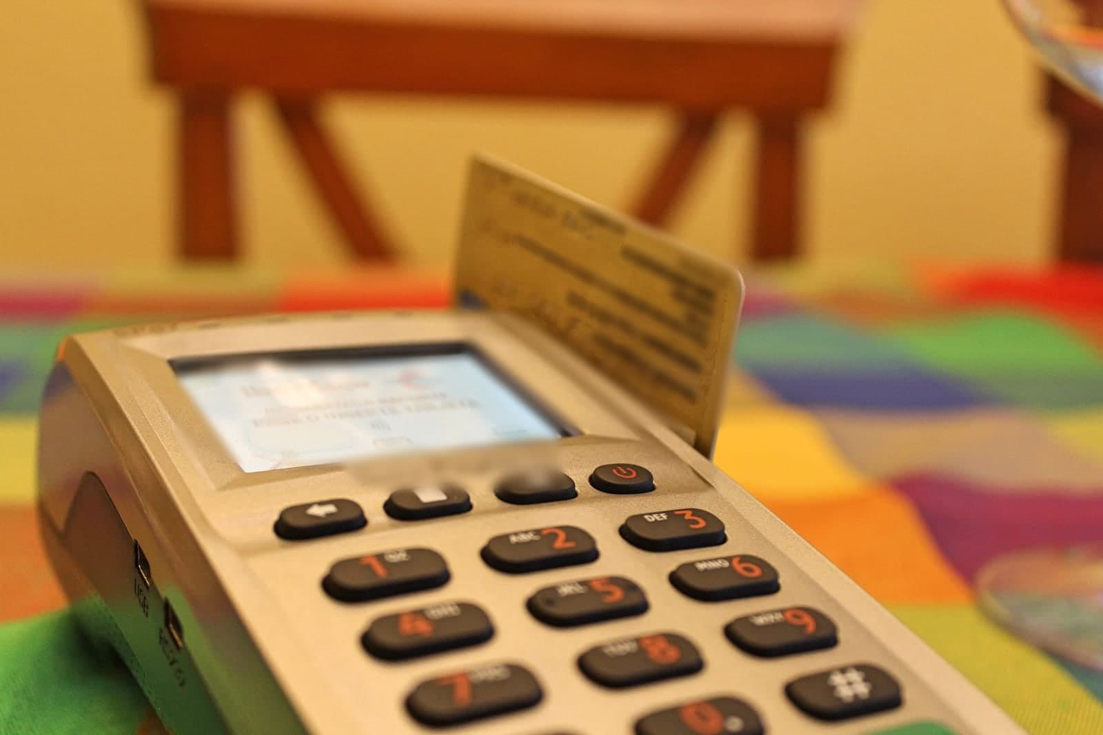 A bank card sits in a card reader on a table covered with a bright checked cloth
