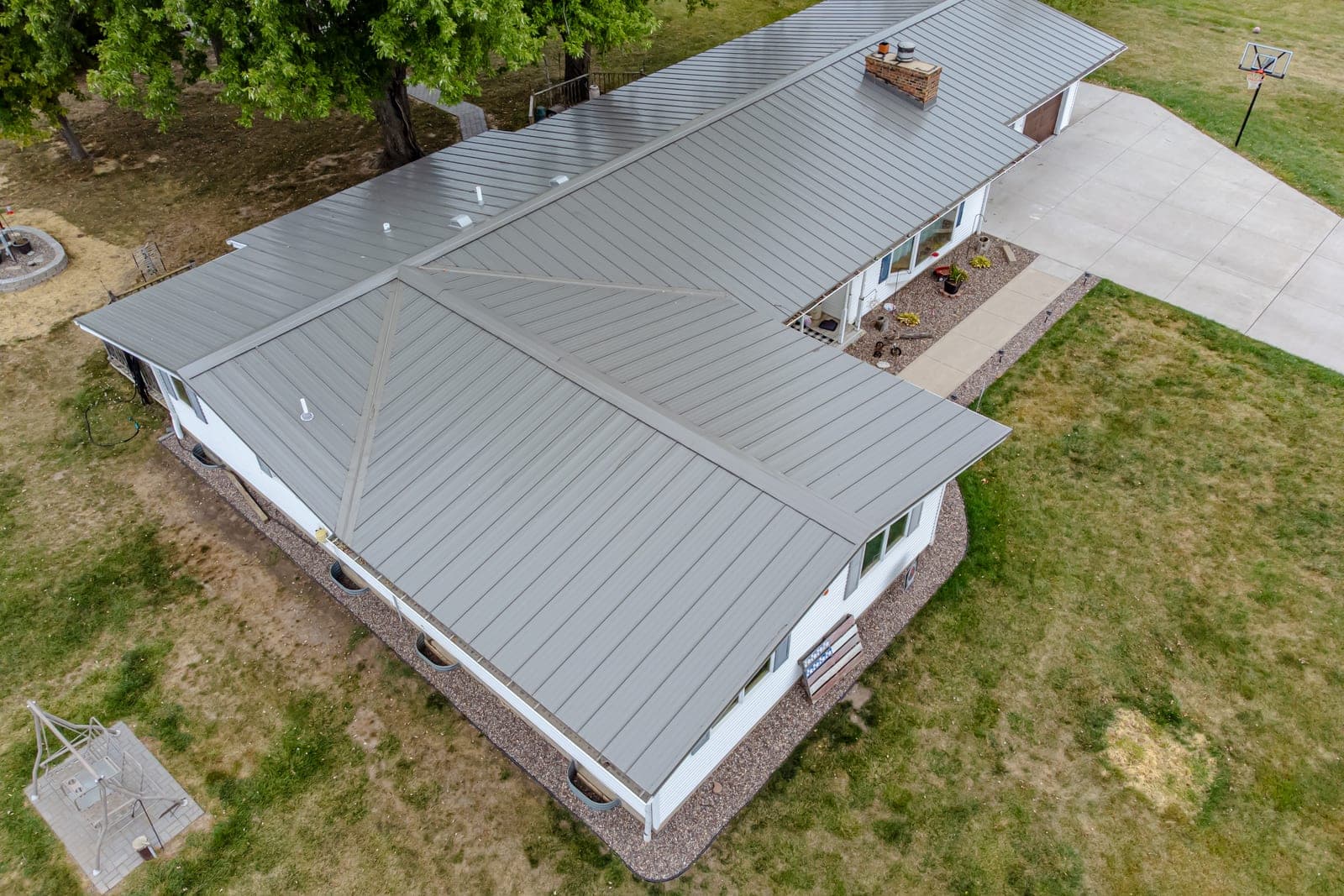 An aerial view of a ranch-style house with a new gray standing seam metal roof, surrounded by lawn