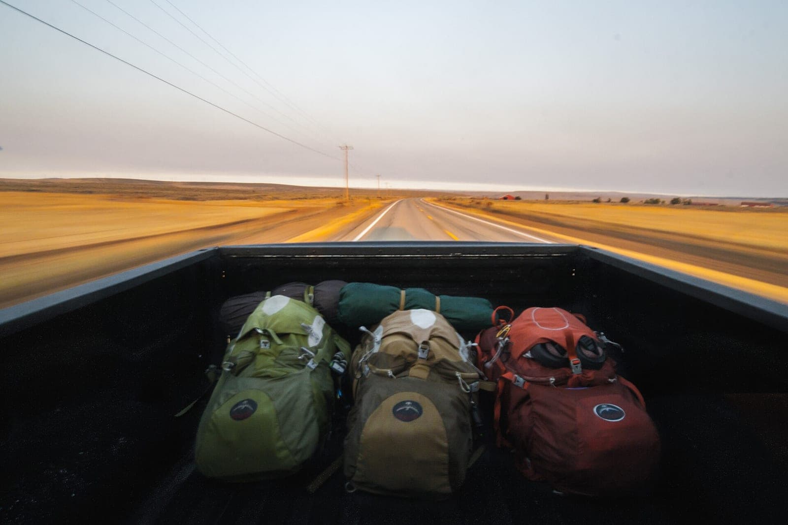 Three backpacks in a pickup truck bed on an open country road