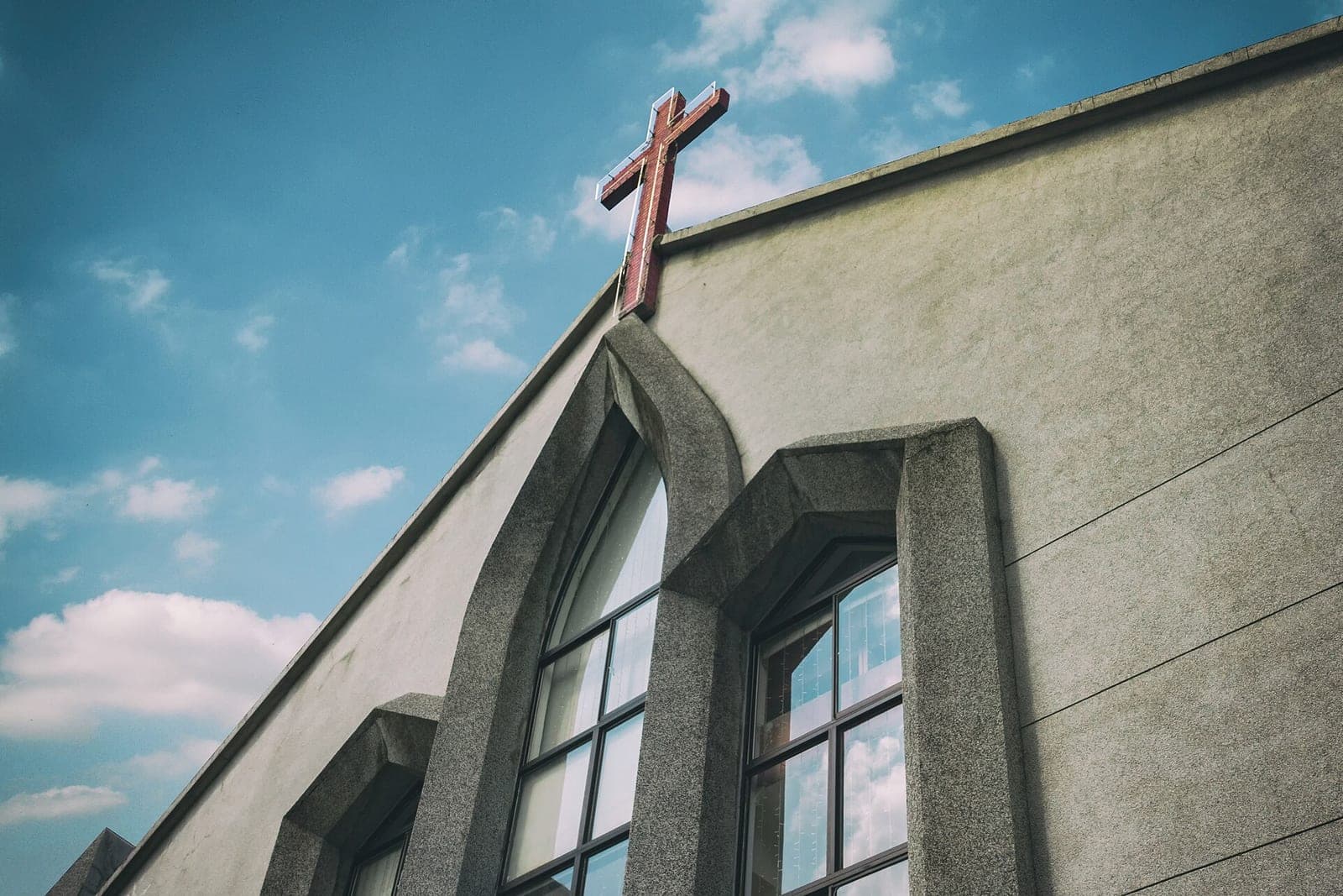 The cross on the gable of a modern church with tall pointed windows under a blue sky