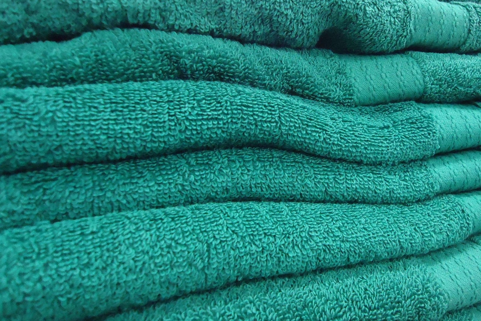 A close stack of soft teal bath towels folded neatly on top of each other