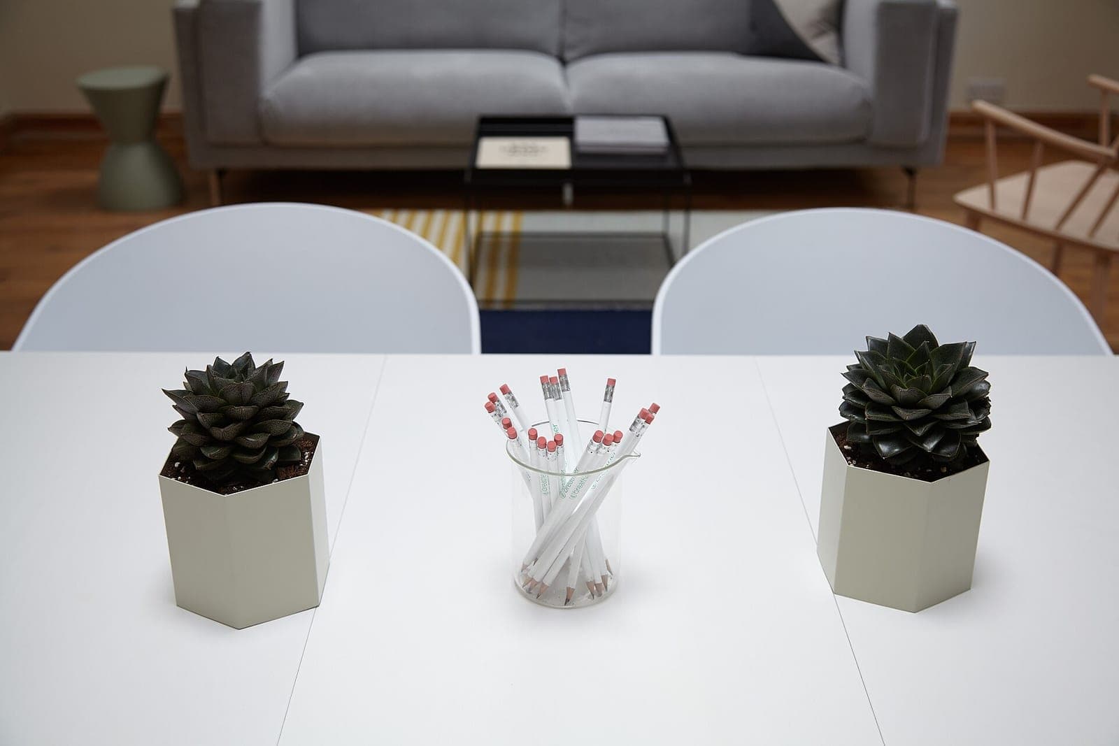 Two potted succulents and a glass of white pencils on a white meeting table, with a gray sofa behind