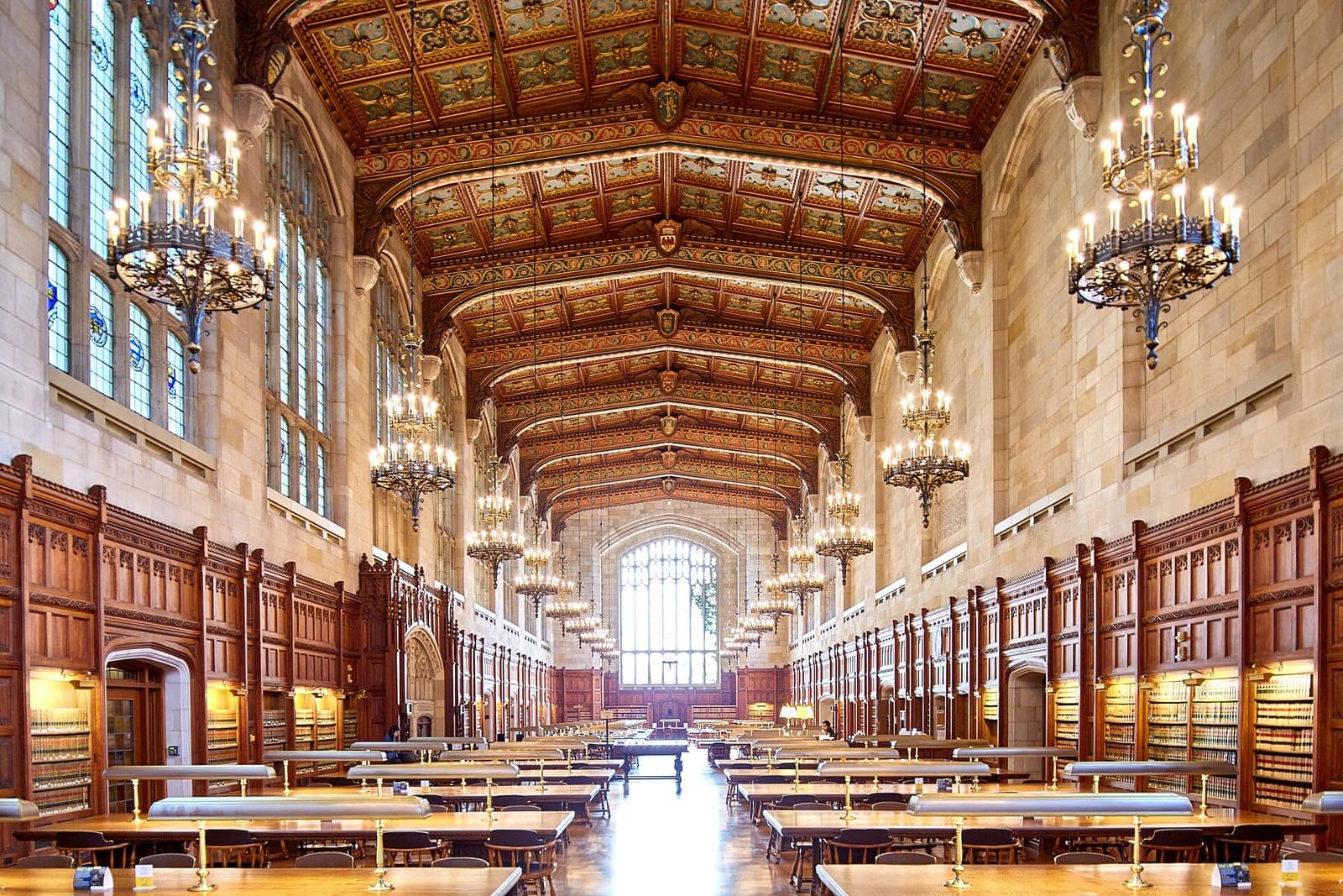 A long law library reading room with wooden tables, brass reading lamps and hanging chandeliers